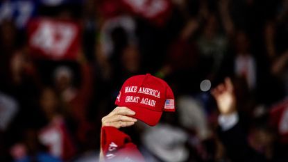 An elderly woman holds up a red MAGA hat