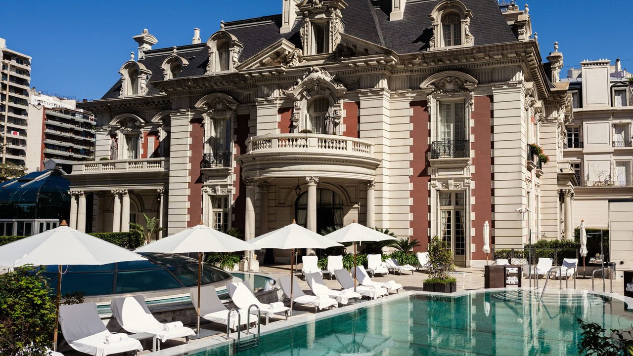 Image of the outside of Four Seasons Buenos Aires. There is a pool with white lounge chairs and white pool umbrellas.