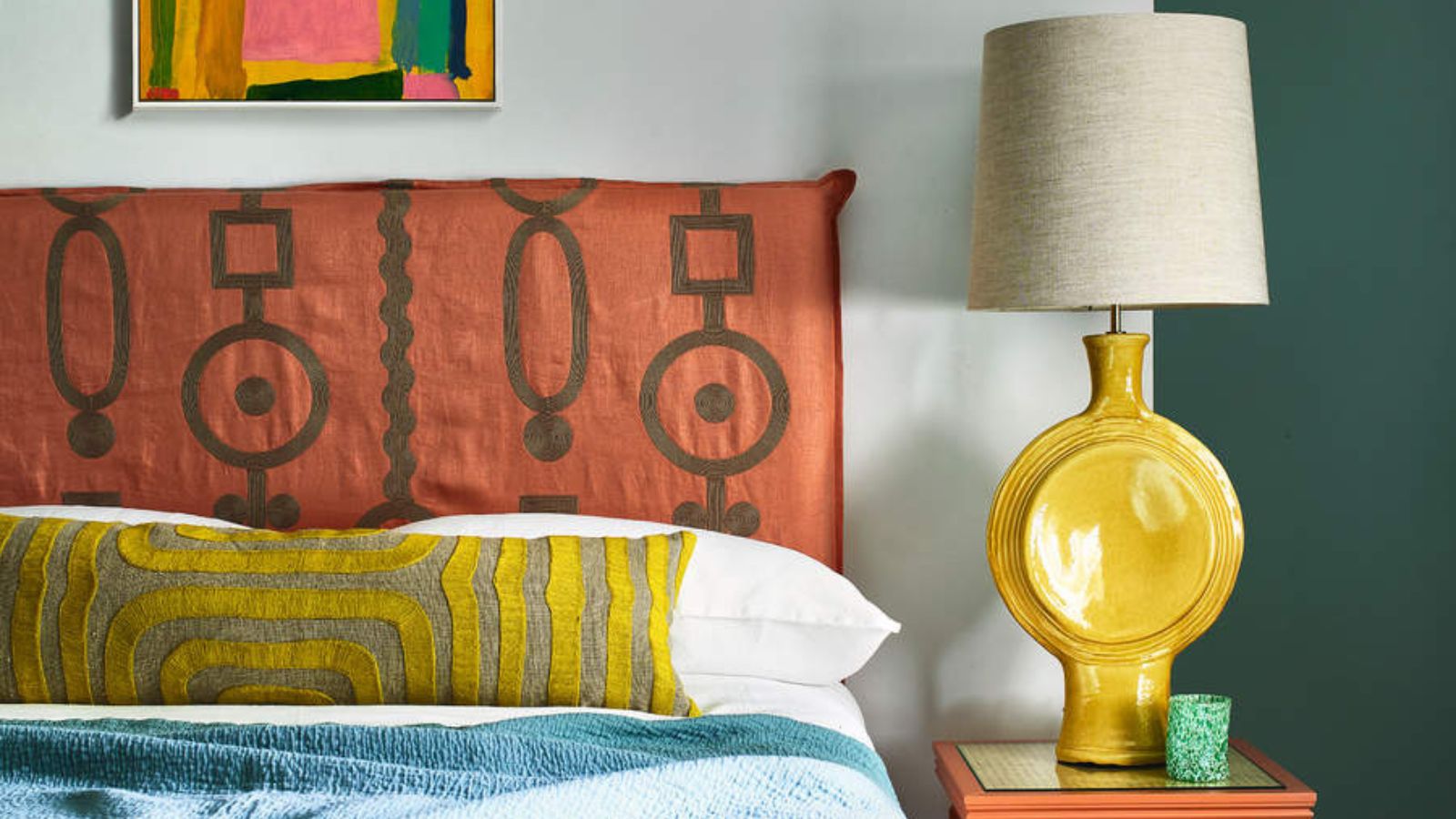 Yellow and blue bedding on an orange bed frame against pale blue walls; to the right, a yellow lamp on a nightstand. 