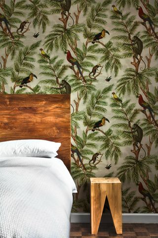 Jungle print wallpaper with wildlife behind wooden headboard with solid wood side table stool
