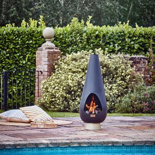 paved area by swimming pool in garden with chiminea style fire, cushions and tray