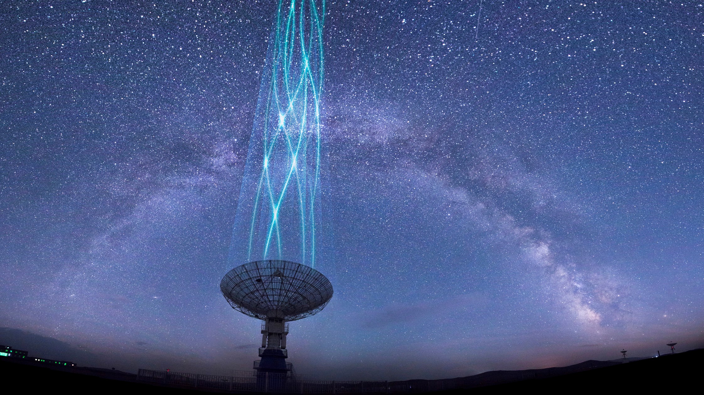 Radio telescope dish pointing at the sky. Milky way band streaks across the sky above.