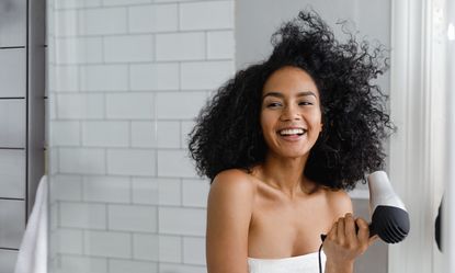 Smiling Young Woman with hair dryer smiling into Mirror