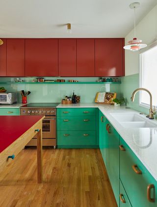 kitchen with green base units and red wall cabinets with red-topped island and white worksurfaces