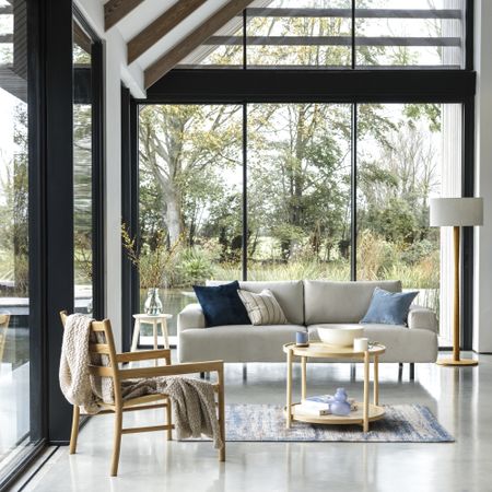 A cream sofa and wooden chair in a living area with glass walls