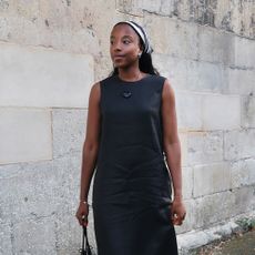 a woman wearing a black linen dress, red sandals, a black bag, and a black-and-white headscarf