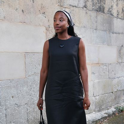 a woman wearing a black linen dress, red sandals, a black bag, and a black-and-white headscarf