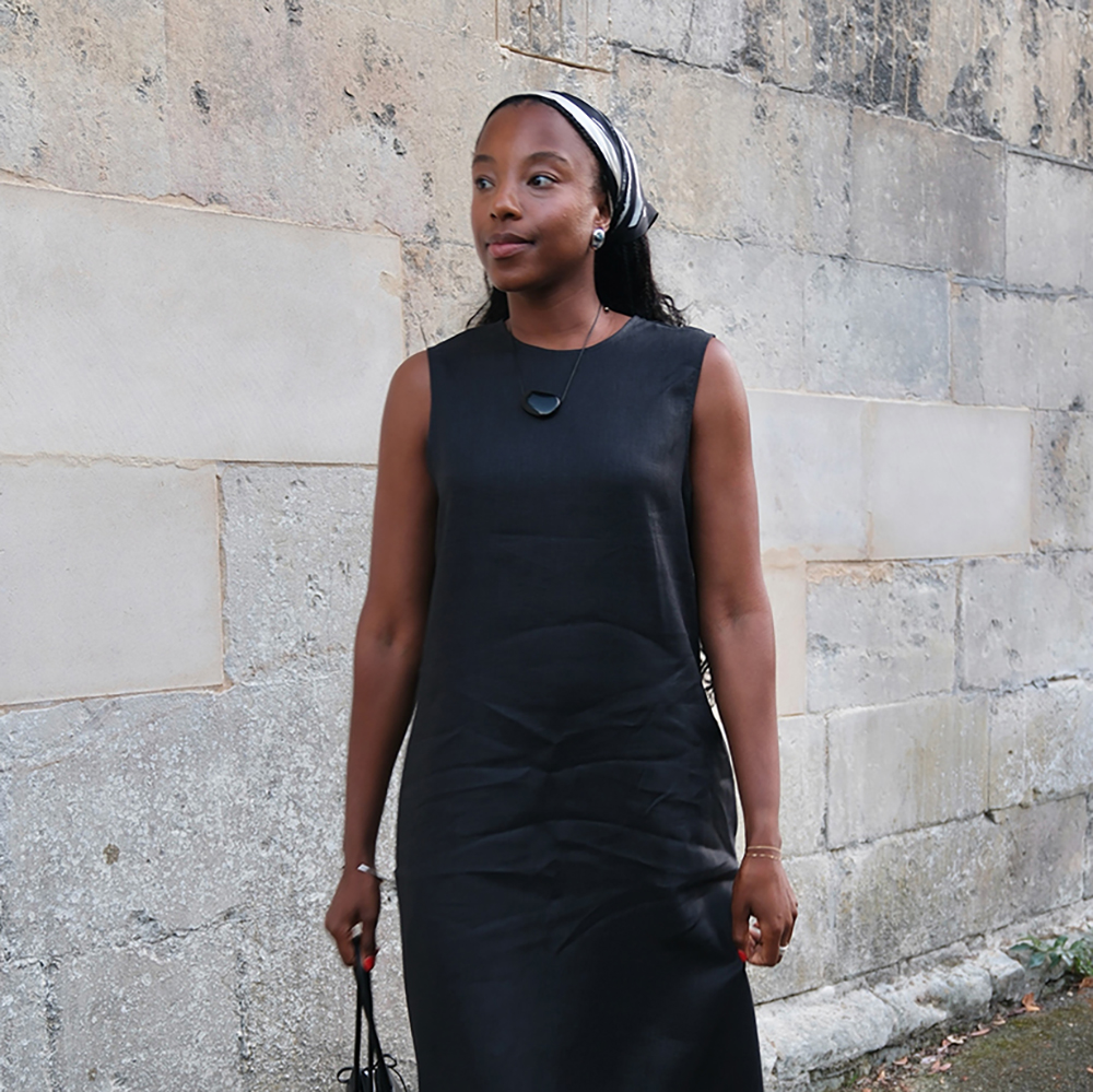 a woman wearing a black linen dress, red sandals, a black bag, and a black-and-white headscarf