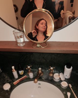 @emmahoareau taking a selfie in a bathroom mirror with lots of skincare products on the sink