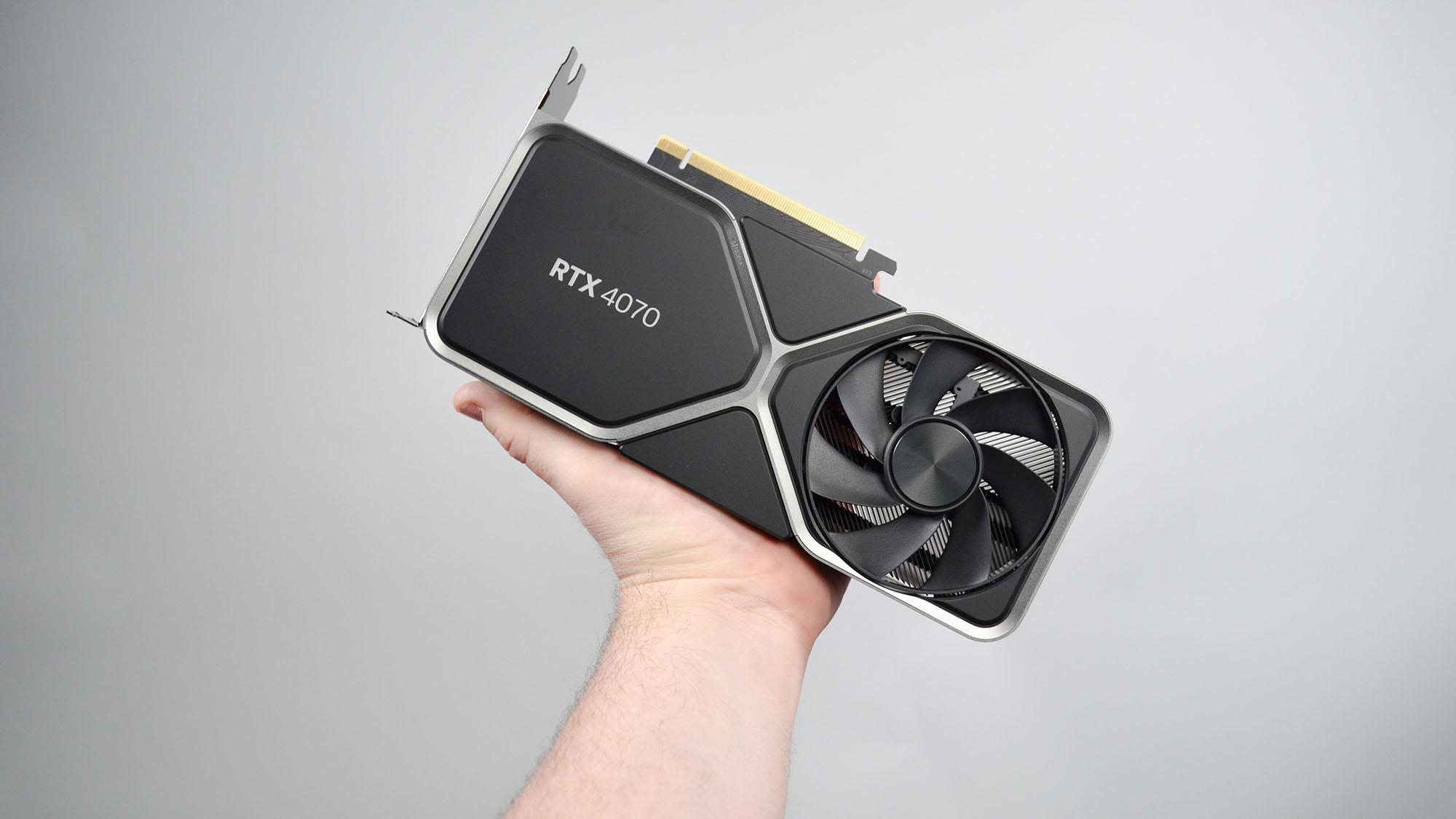 A man's hand holding the Nvidia GeForce RTX 4070 graphics card