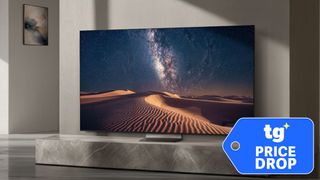 The Samsung R95H in a gray-colored living room displaying the Milky Way over sand dunes in the desert