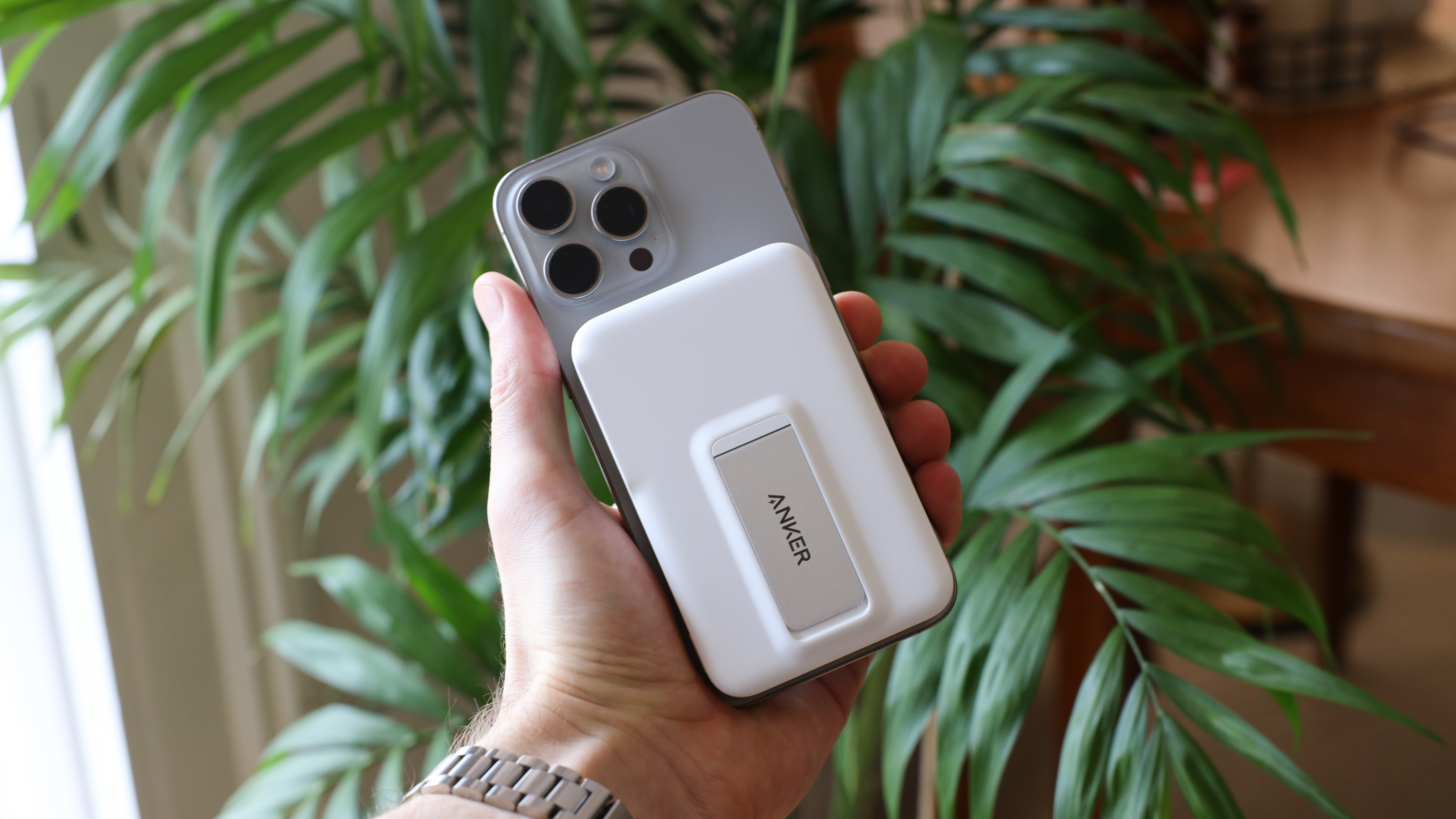 باور بانك Anker MagGo (10K) متصل بجهاز iPhone 15 Pro Max ومثبت في اليد أمام نبات أخضر