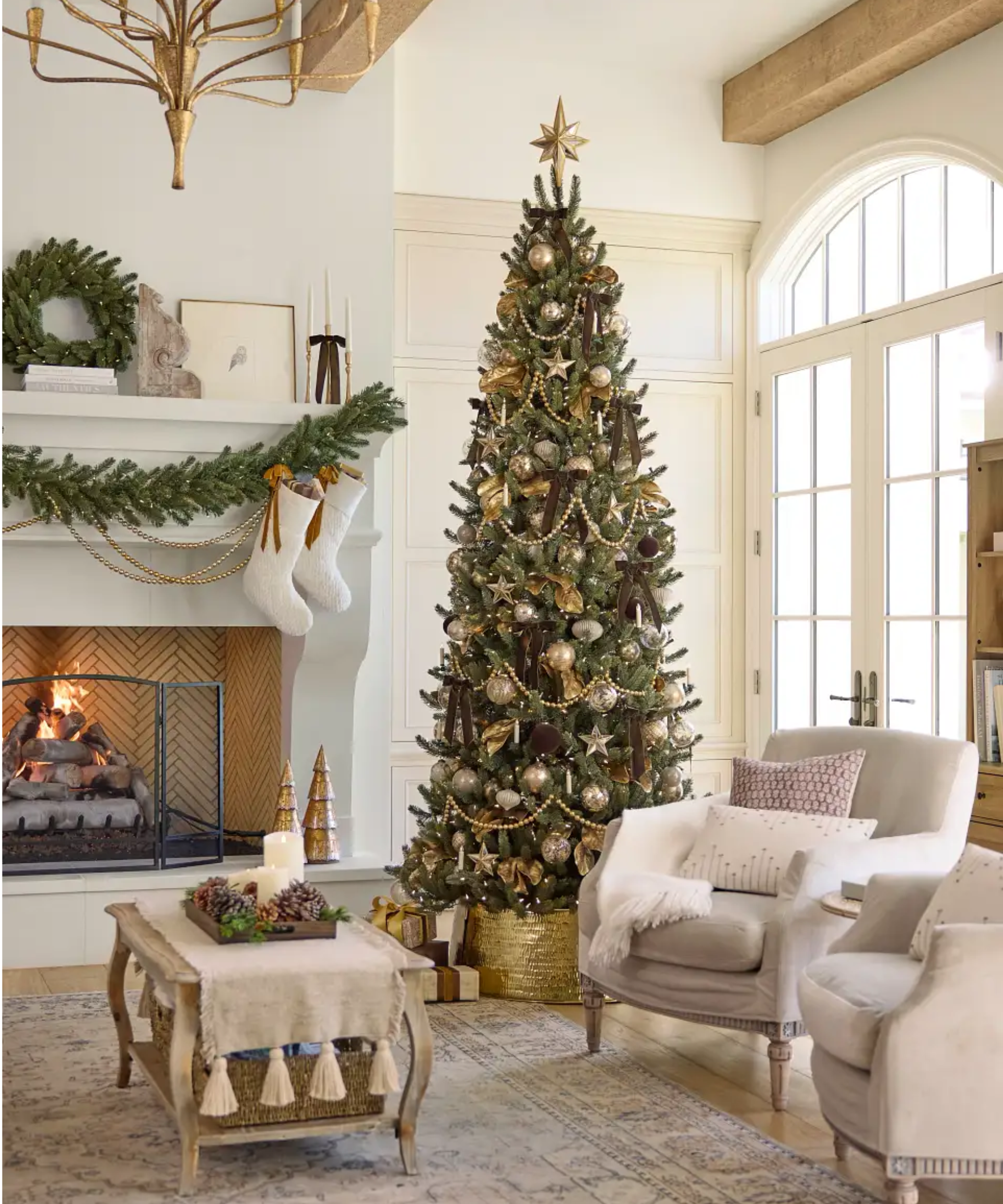 Opulently decorated Christmas living room featuring a grand 9 ft tree dressed in gold and silver ornaments and garland, alongside antique-style armchairs, a cof