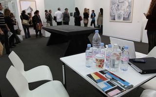 Water bottles on a white table in a room filled with people looking at art against walls