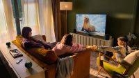A photograph of a family watching TV, with four HomePod speakers dotted around the room for sound