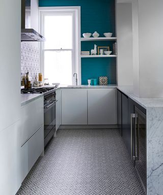 Galley kitchen with patterned floor tiles and backsplash and teal feature wall