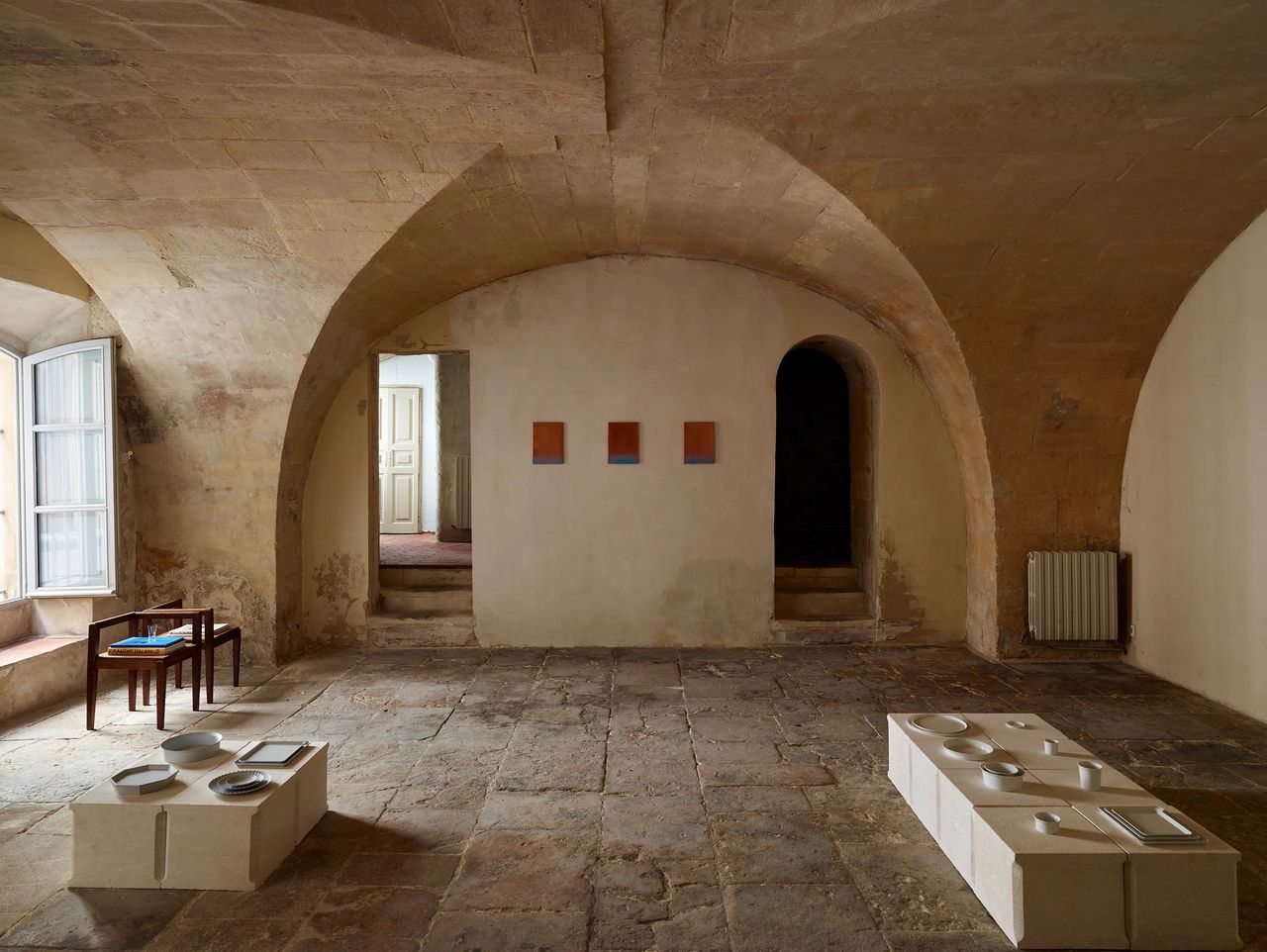 A design showroom set inside an ancient chapel boasts arched stone walls and organic ceramic collectibles across two white podiums.