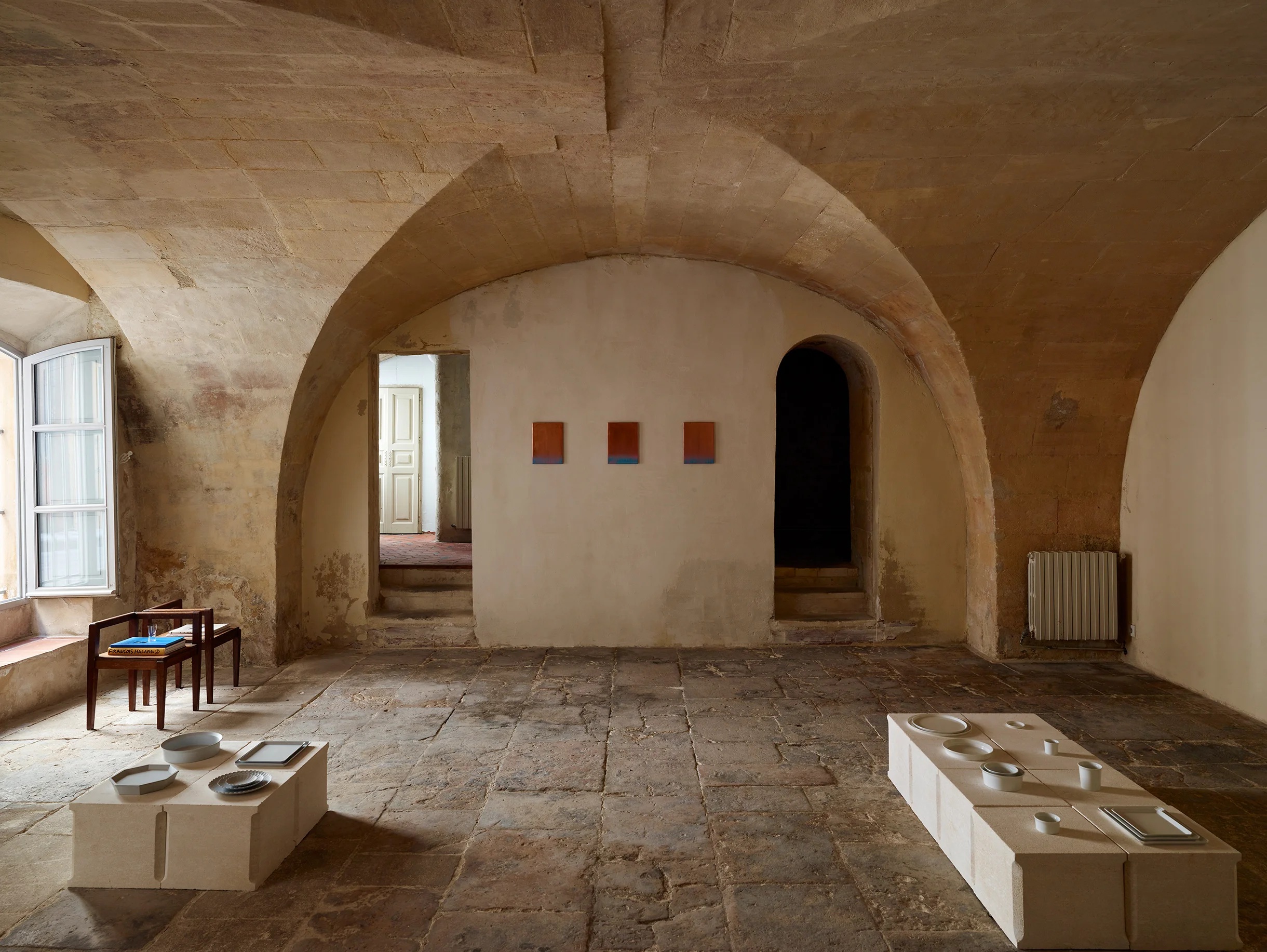 A design showroom set inside an ancient chapel boasts arched stone walls and organic ceramic collectibles across two white podiums.