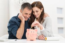 Portrait Of Happy Couple Inserting Coin In Piggybank
