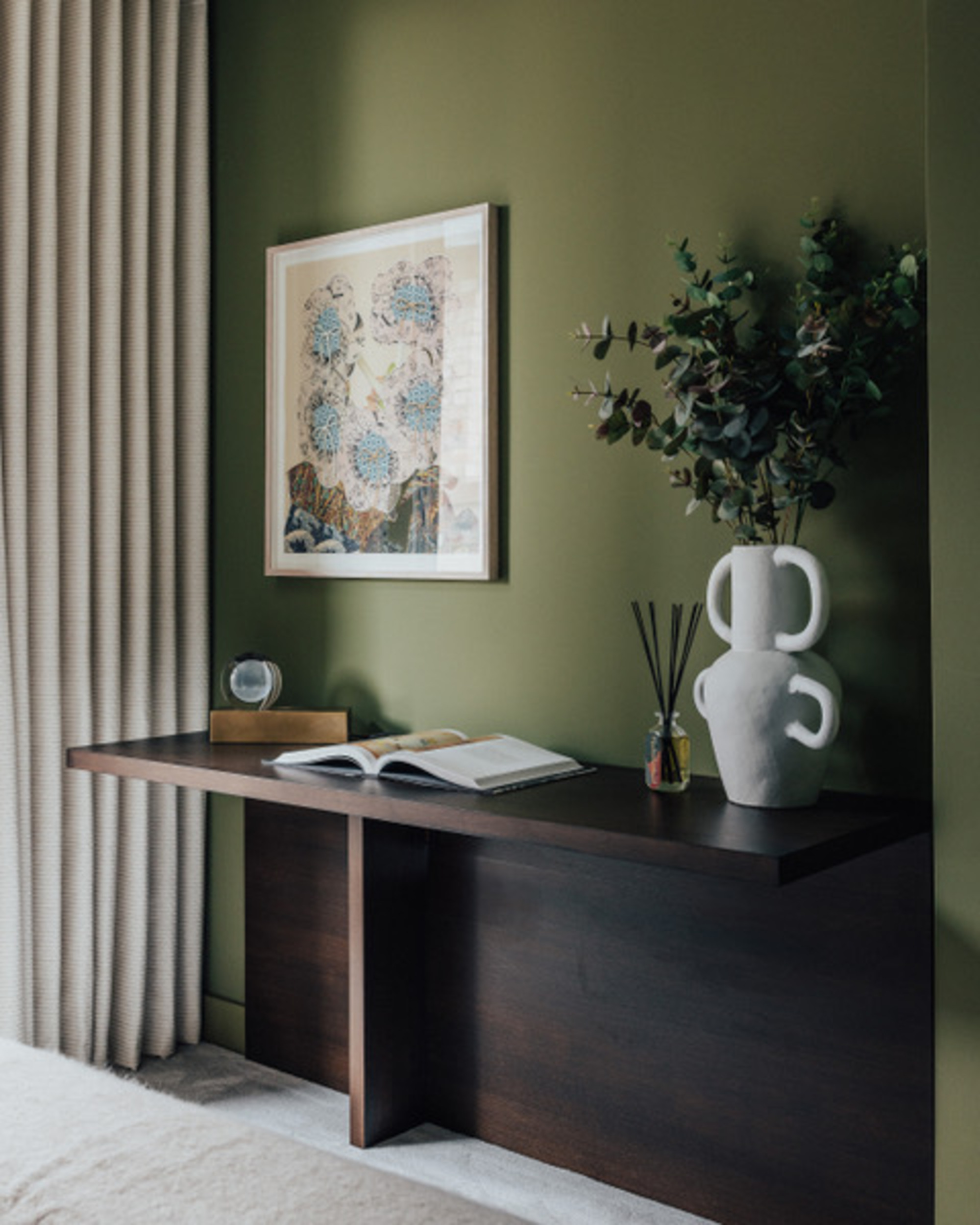 hallway with timber console, open book, vase with branches, scent diffuser, framed artwork, and deep green paint on wall
