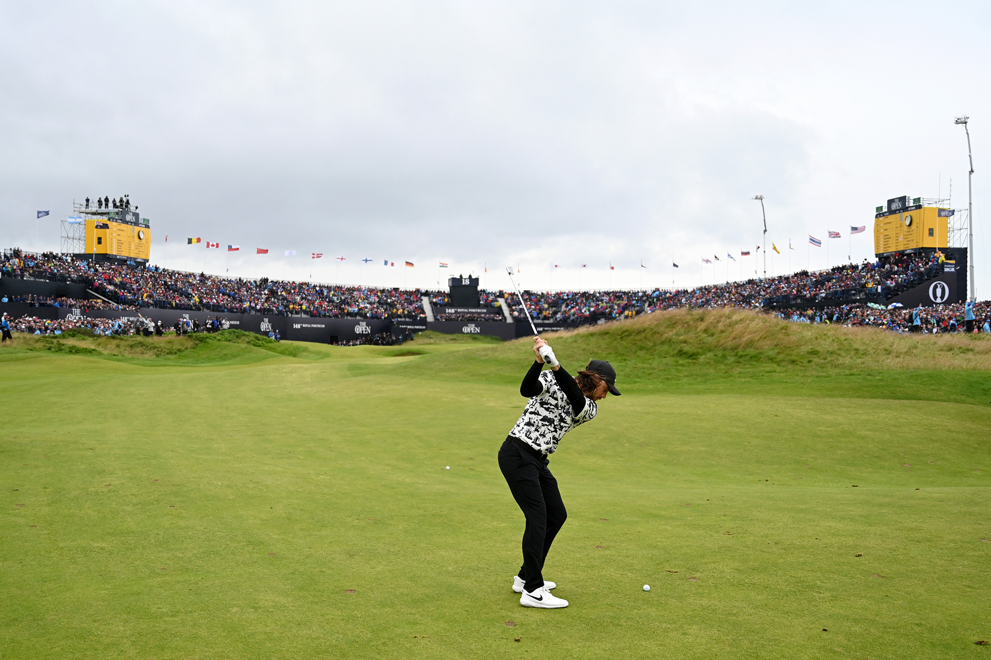 Tommy Fleetwood playing his approach shot into the 18th green during the 2019 Open Championship at Royal Portrush, with a packed grandstand behind the green