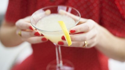 Woman in red with red nail polish holding alcoholic drink with a slice of lemon garnished on the rim of the glass