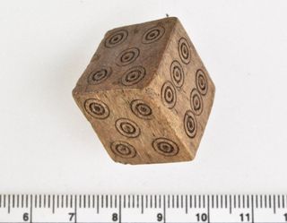 The wooden dice has two 4s and two 5's but no 1 or 2. Archaeologists believe that it was likely used to cheat while gambling. This photo shows the two 4's. 