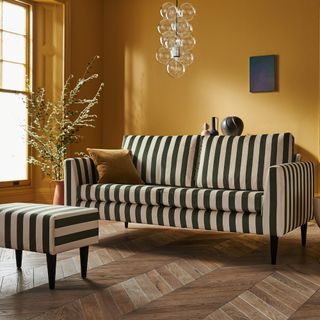 Sofa.com's Jude 3 Seater Sofa and Footstool in striped velvet in a mustard yellow-painted living room with parquet floors