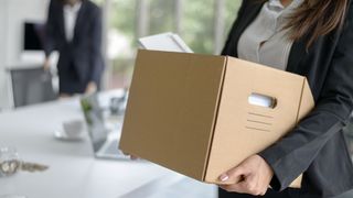 A woman holding a box full of work possessions having left her job