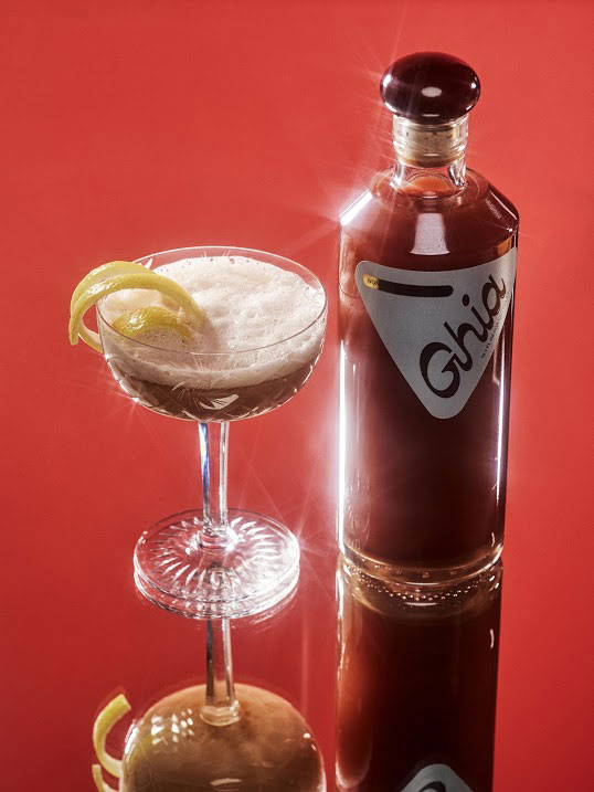 ghia red non-alcoholic drink against red background and next to cocktail glass
