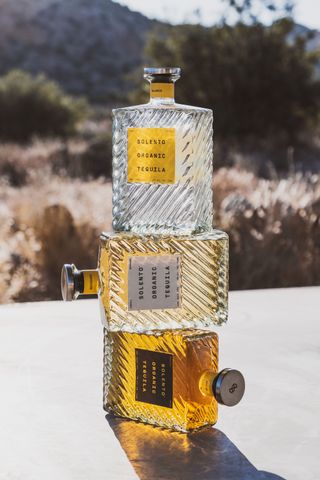 Three bottles of Solento tequila stacked on top of one another on a light coloured surface outside during the day