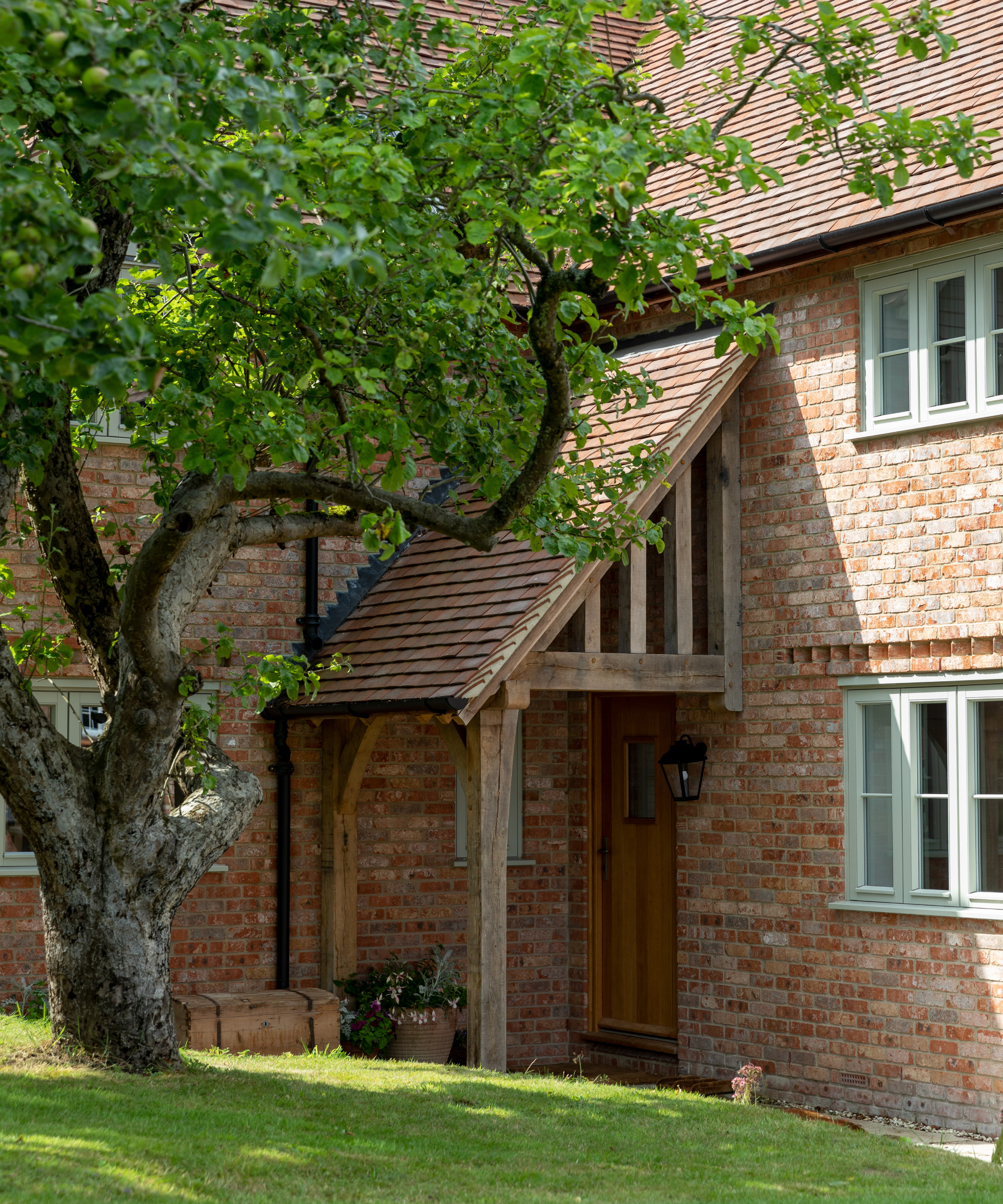 oak framed porch on Lshaped house with corner entranace, sloped tiled roof and porch roof reaching to second storey height of home