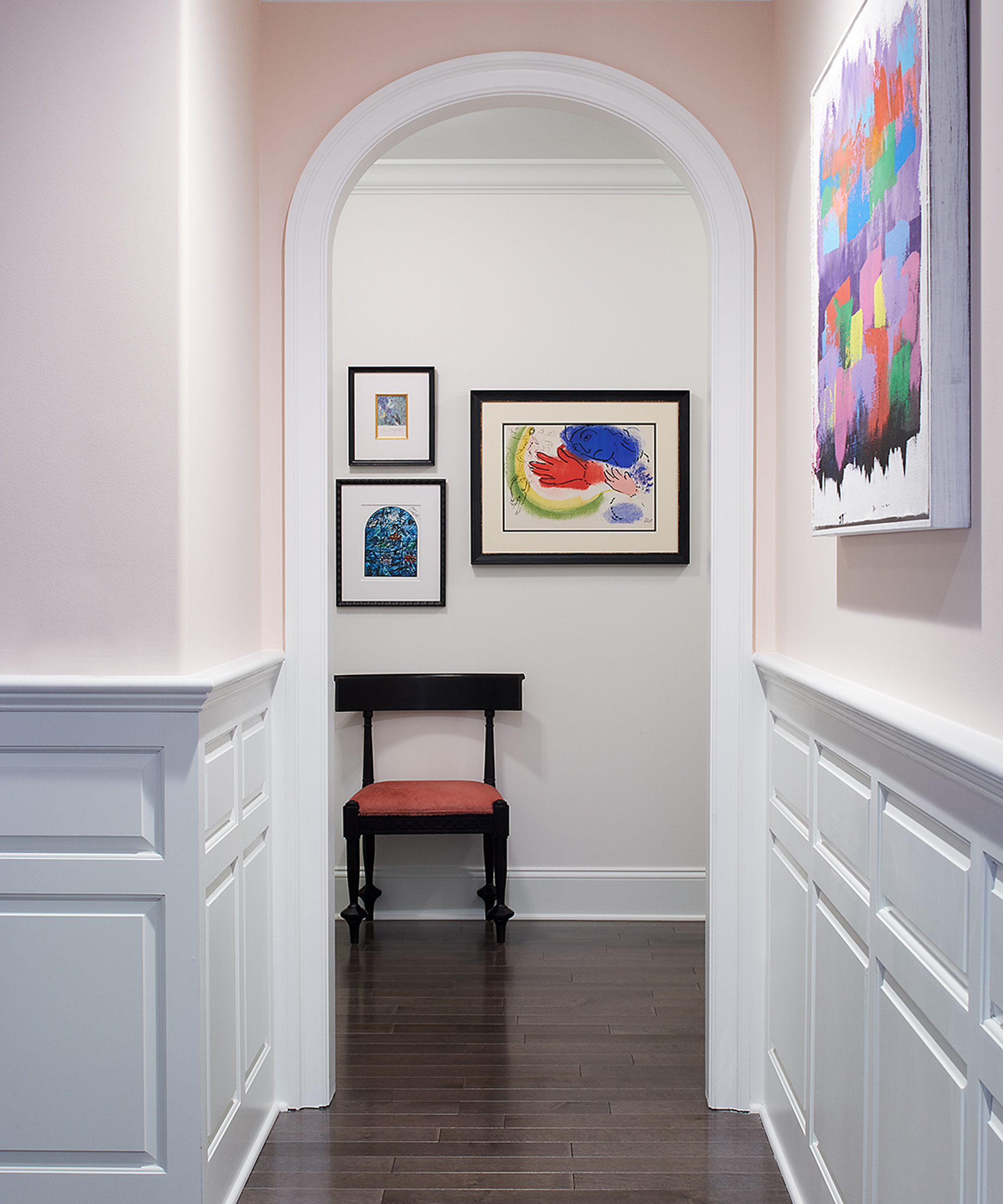 Hallway with arched walkthrough, dark wood flooring, half wall paneling, and modern framed artwork on walls.