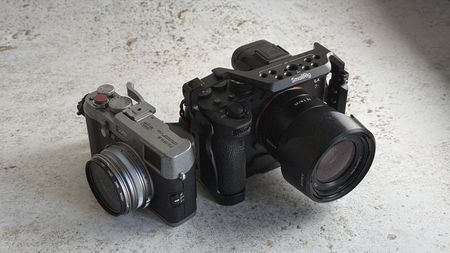 A Fujifilm X100 and a Sony A7Riv on a table top.