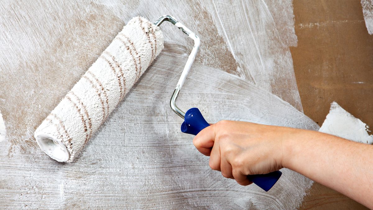 Hand with roller applying paint to wall