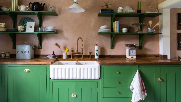 Playful and colorful kitchen with bright green painted cabinets and coordinating shelves, and large ceramic sink with aged brass tap