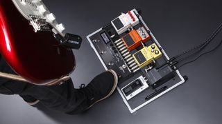 Man holding red guitar, with wireless system attached, puts his foot on his pedalboard