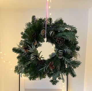 Traditional wreath with dried limes and pinecones hung over mantel using pink satin ribbon
