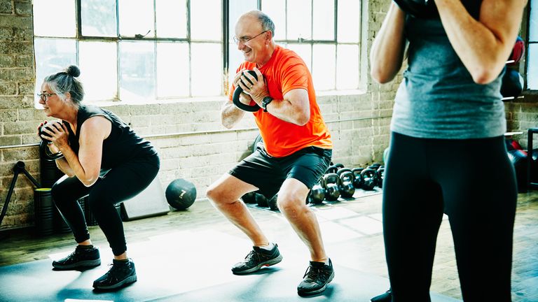 Older workout class squat while carrying a kettlebell