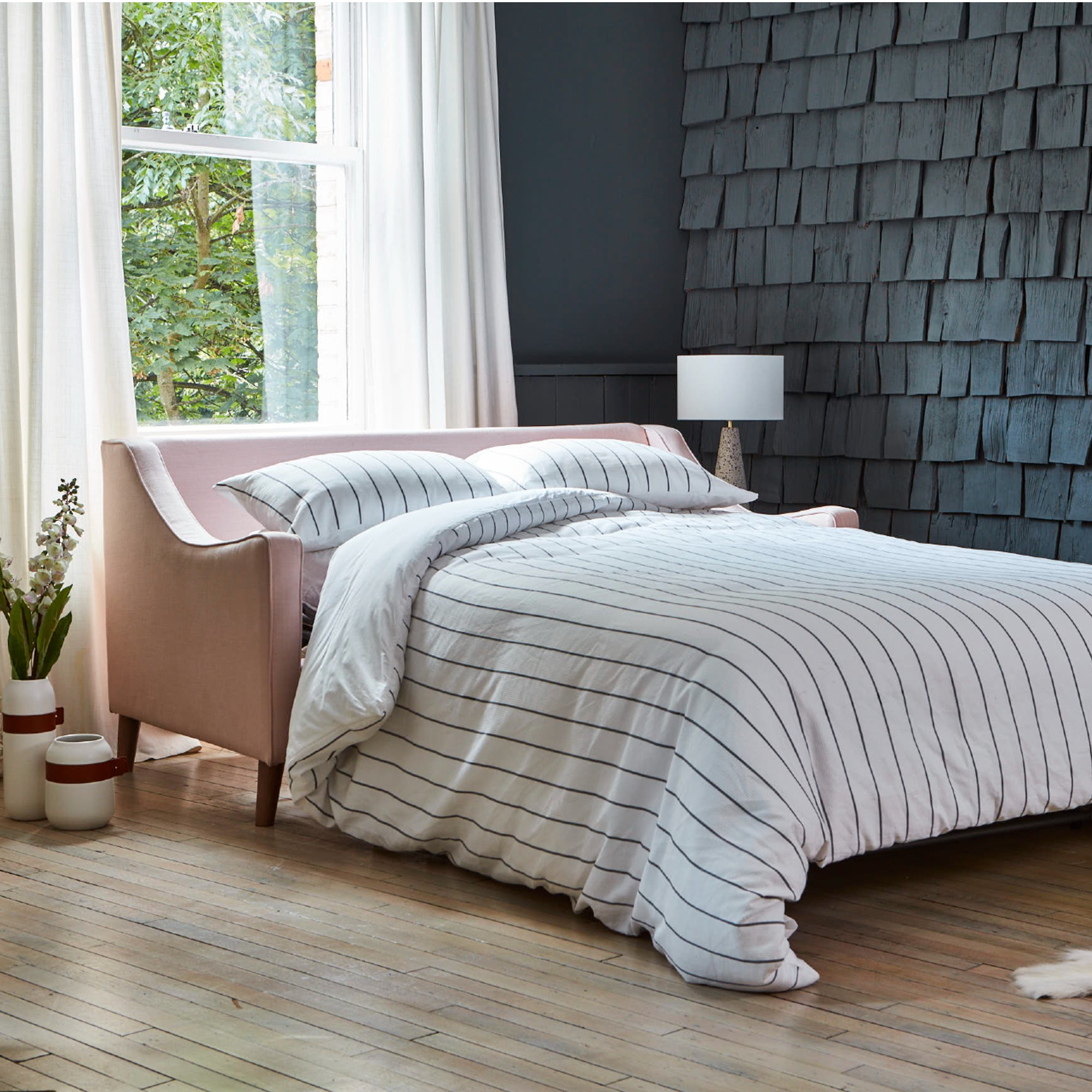 A pink pull-out sofa bed in a living room with a dark grey feature wall