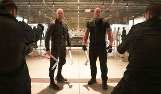 Hobbs & Shaw standing with pipes, as guns are drawn on them in the secret base