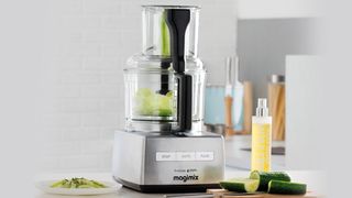 A Magimix food processor on a kitchen countertop surrounded by fresh produce