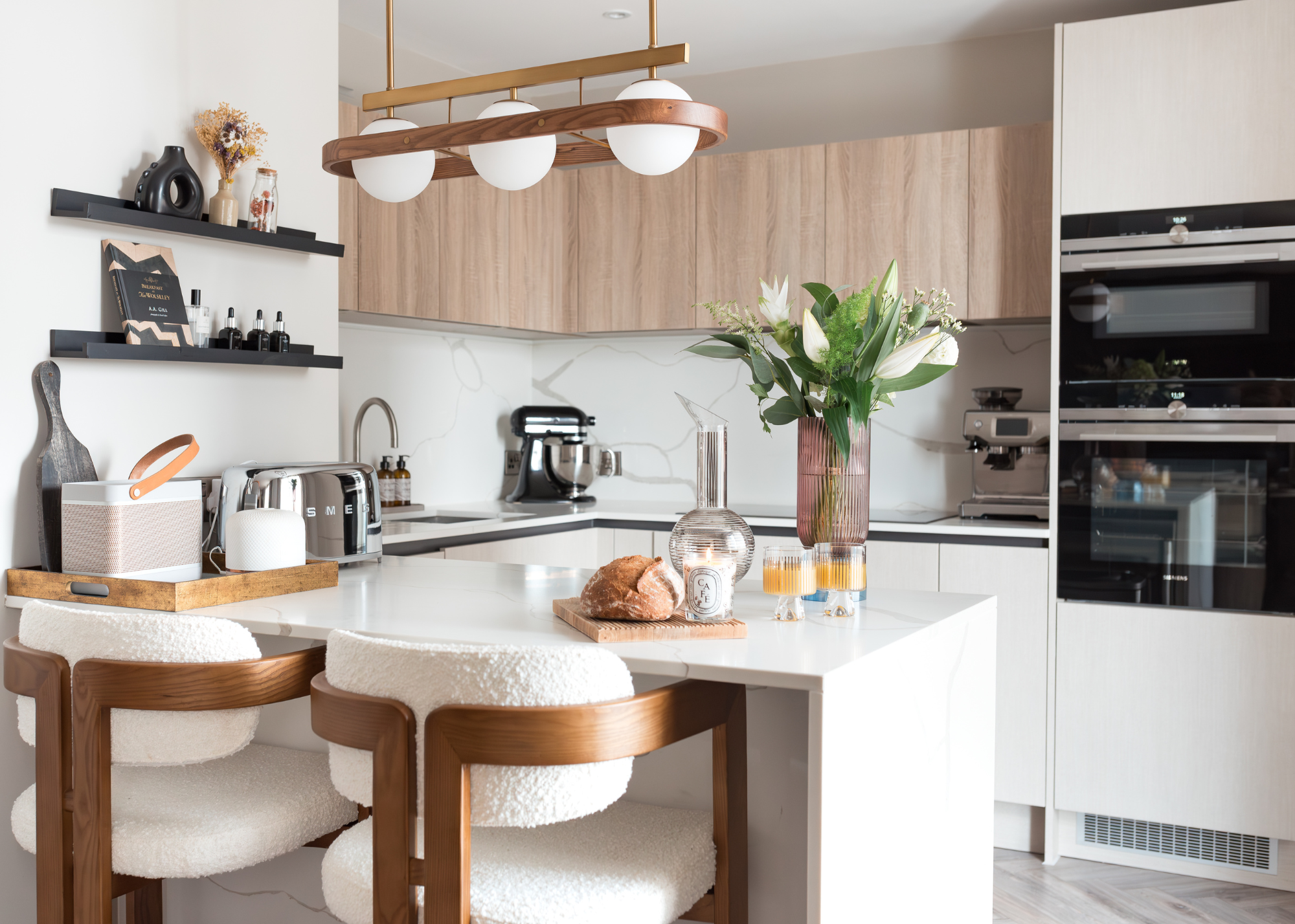 A small light white and wood kitchen with a peninsula island and two neat boucle and wood bar stools at the breakast bar