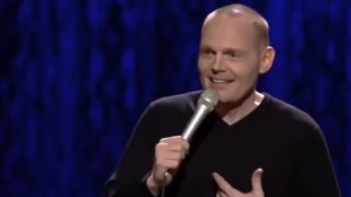 Bill Burr wearing a black sweater telling a joke.