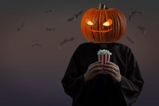 Pumpkin head person holding movie theatre popcorn.