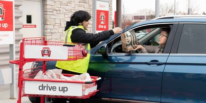 A Starbucks employee hands a bag to a woman in a car at a Target Drive Up