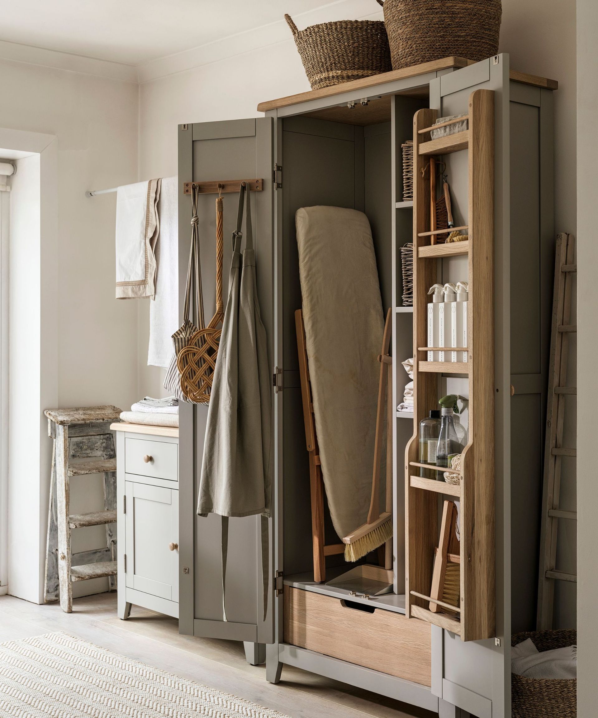 An open wooden storage cabinet filled with non-toxic cleaning supplies and an ironing board.