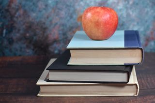 An apple on top of books in front of a blackboard.