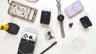 Various phone accessories including power banks, cases, stands, grips, earbuds, smartwatches, and more spread out on a table.
