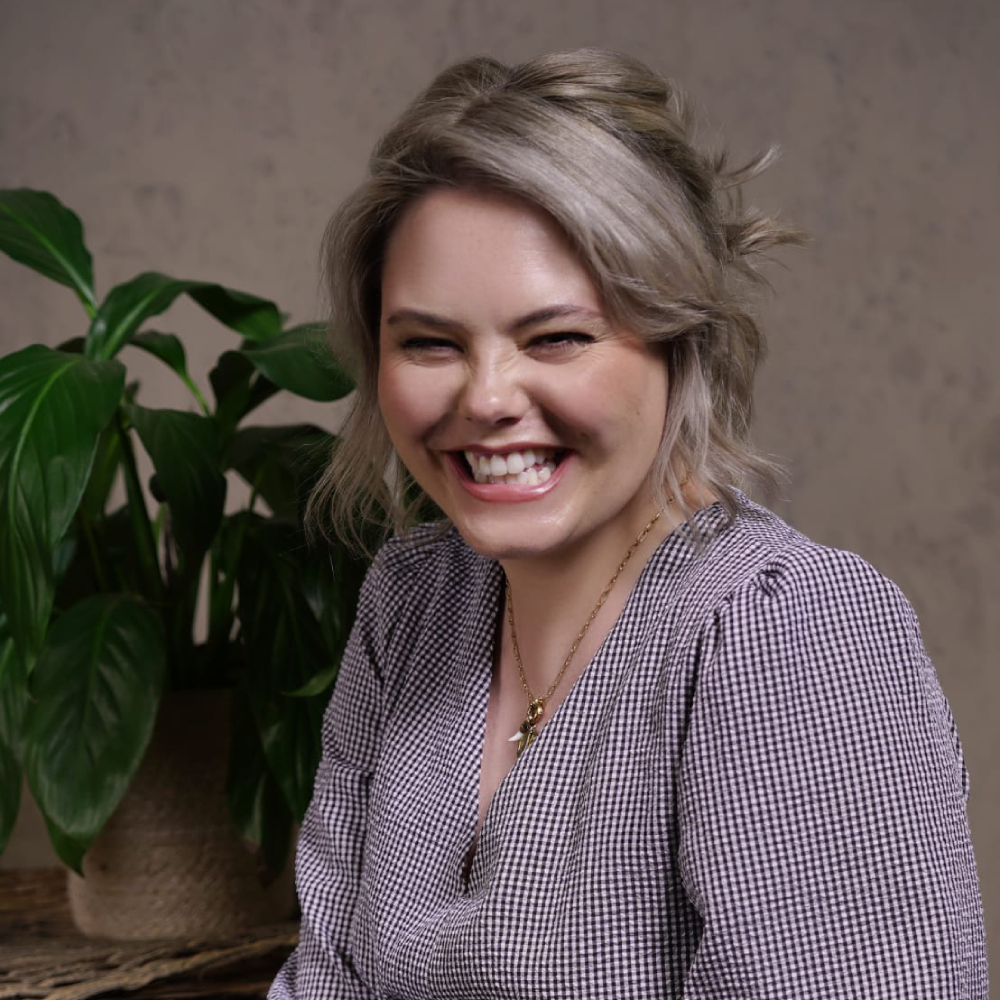 female with short blond hair wearing checked blouse sat smiling